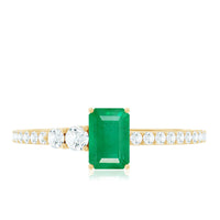 Natural emerald cut emerald engagement ring with diamond side stones, featuring a sleek gold band and detailed craftsmanship.