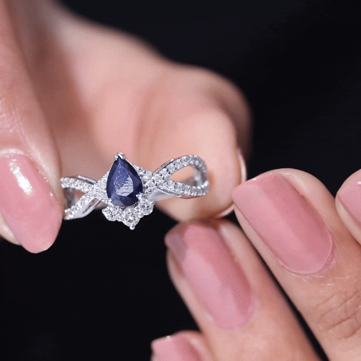 Pear-shaped blue sapphire engagement ring with diamond crossover design by Rosec Jewels, showcasing a sparkling blue sapphire and diamond accents.