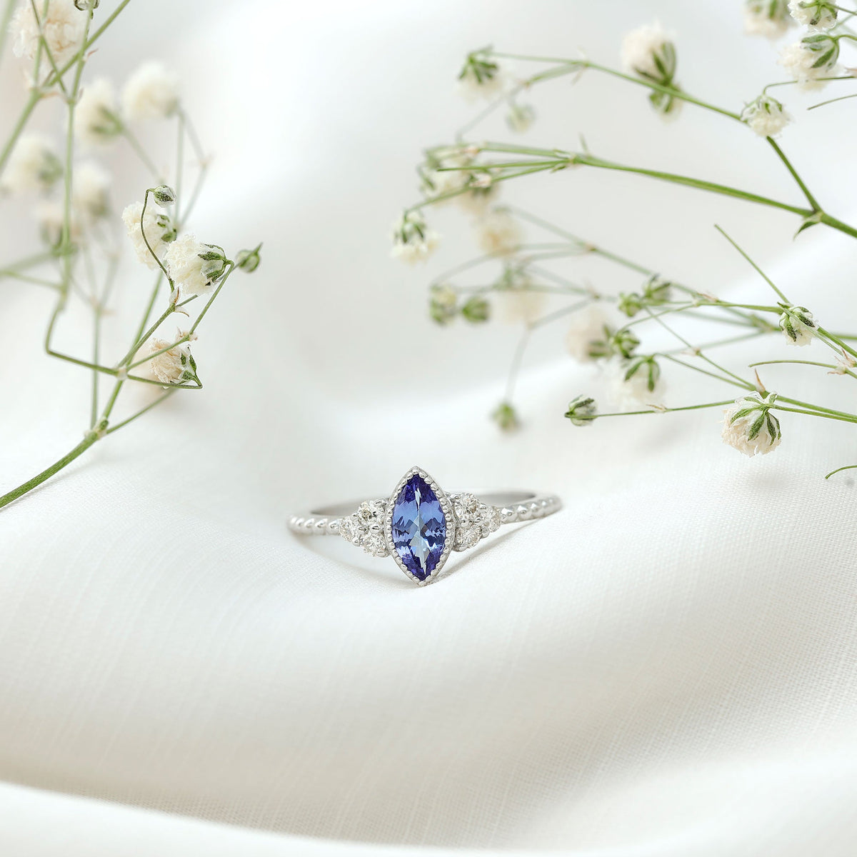 Vintage style marquise tanzanite promise ring with diamond trio, featuring elegant design and intricate metalwork.
