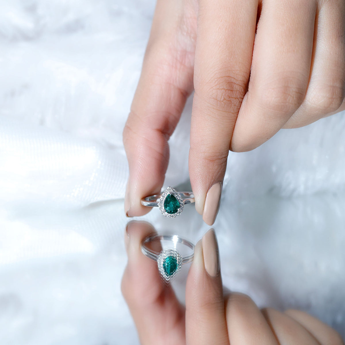 Real emerald teardrop engagement ring with diamond halo, featuring a rose gold band and intricate gemstone detail.