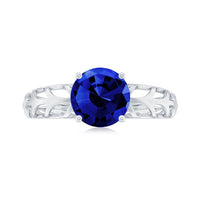 Lab-created blue sapphire solitaire ring with filigree shank by Rosec Jewels, featuring a sparkling blue gemstone and intricate metalwork.