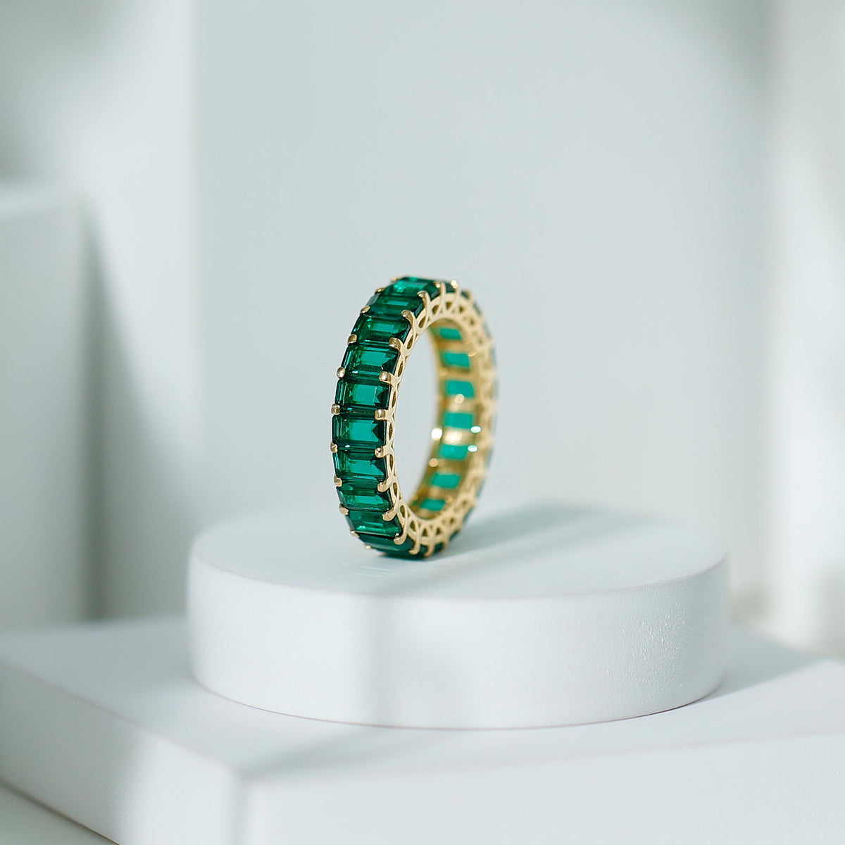 Emerald cut lab-grown emerald eternity wedding band by Rosec Jewels, showcasing a continuous row of sparkling emeralds on a sleek ring.