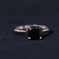 Black onyx solitaire engagement ring with cushion cut center stone, set in a sleek band, by Rosec Jewels.