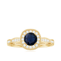 Round 0.9 carat blue sapphire antique engagement ring with diamond halo, featuring intricate gold band and vintage design.