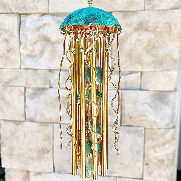 Teal, green, and gold jellyfish wind chime by Alison Morse hanging outdoors with flowing tentacle details.