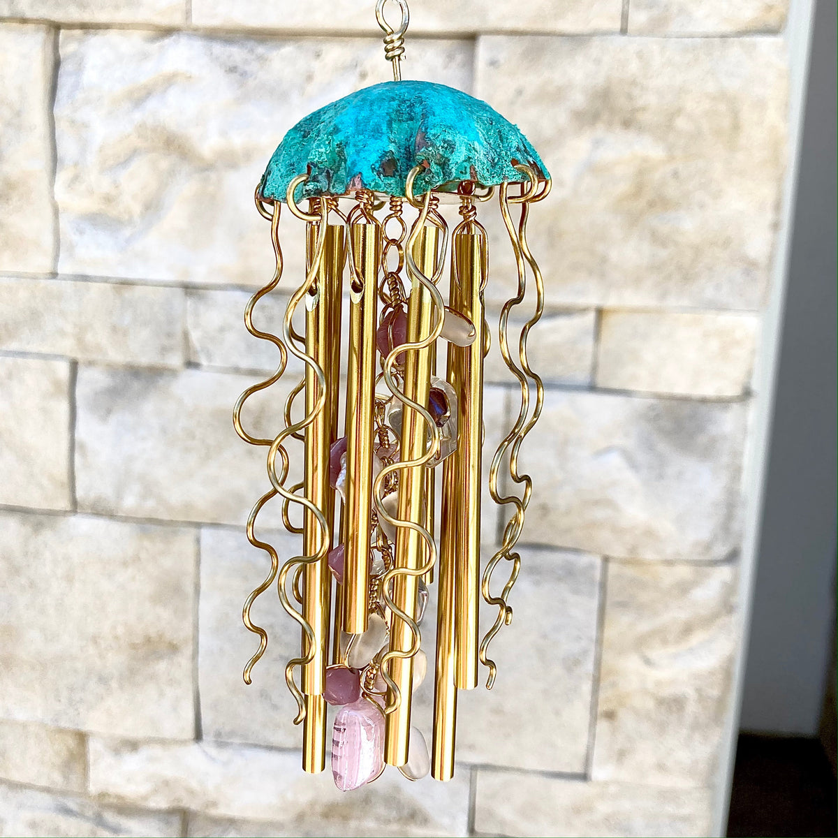 Colorful jellyfish-shaped wind chime by Alison Morse hanging outdoors with ocean-themed design and glass elements.