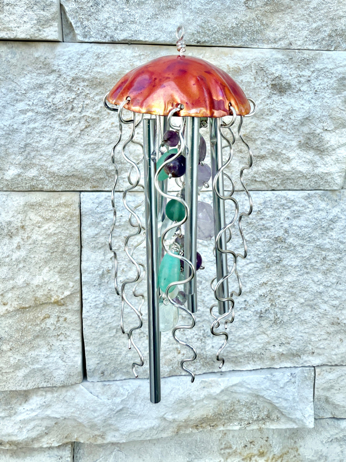 Colorful jellyfish-shaped wind chime by Alison Morse hanging outdoors with ocean-themed design and glass bell details.