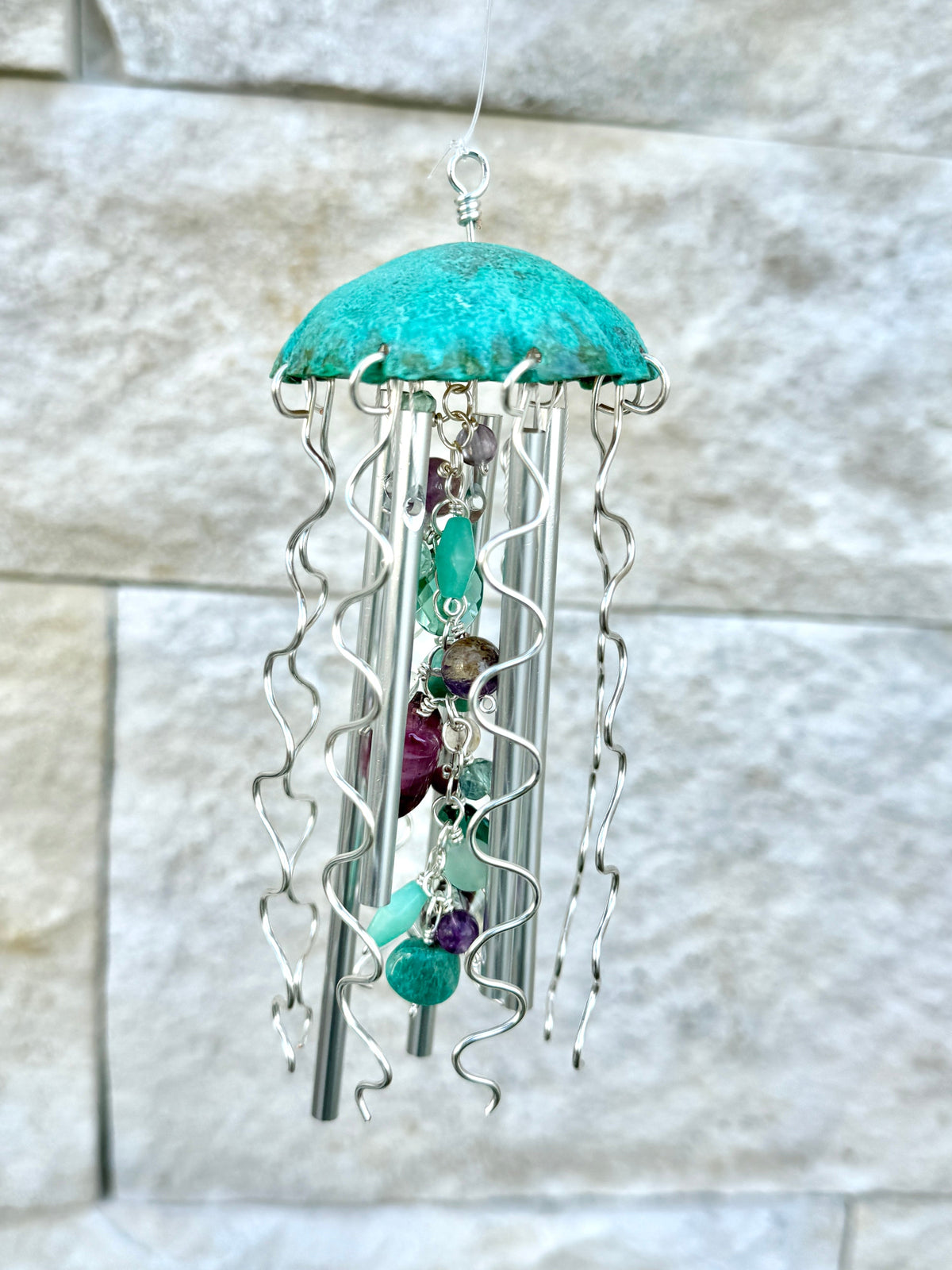Colorful Alison Morse jellyfish wind chime hanging outdoors with glass and metal elements, creating gentle sound and visual appeal.
