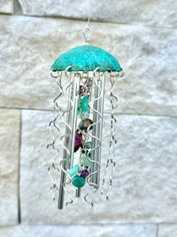 Colorful Alison Morse jellyfish wind chime hanging outdoors with glass and metal elements, creating gentle sound and visual appeal.