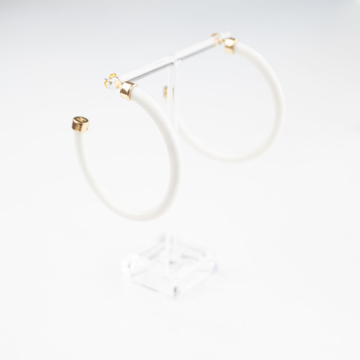 White hoop earrings by hoohoops, showing close-up of sleek circular jewelry on a model's ear.