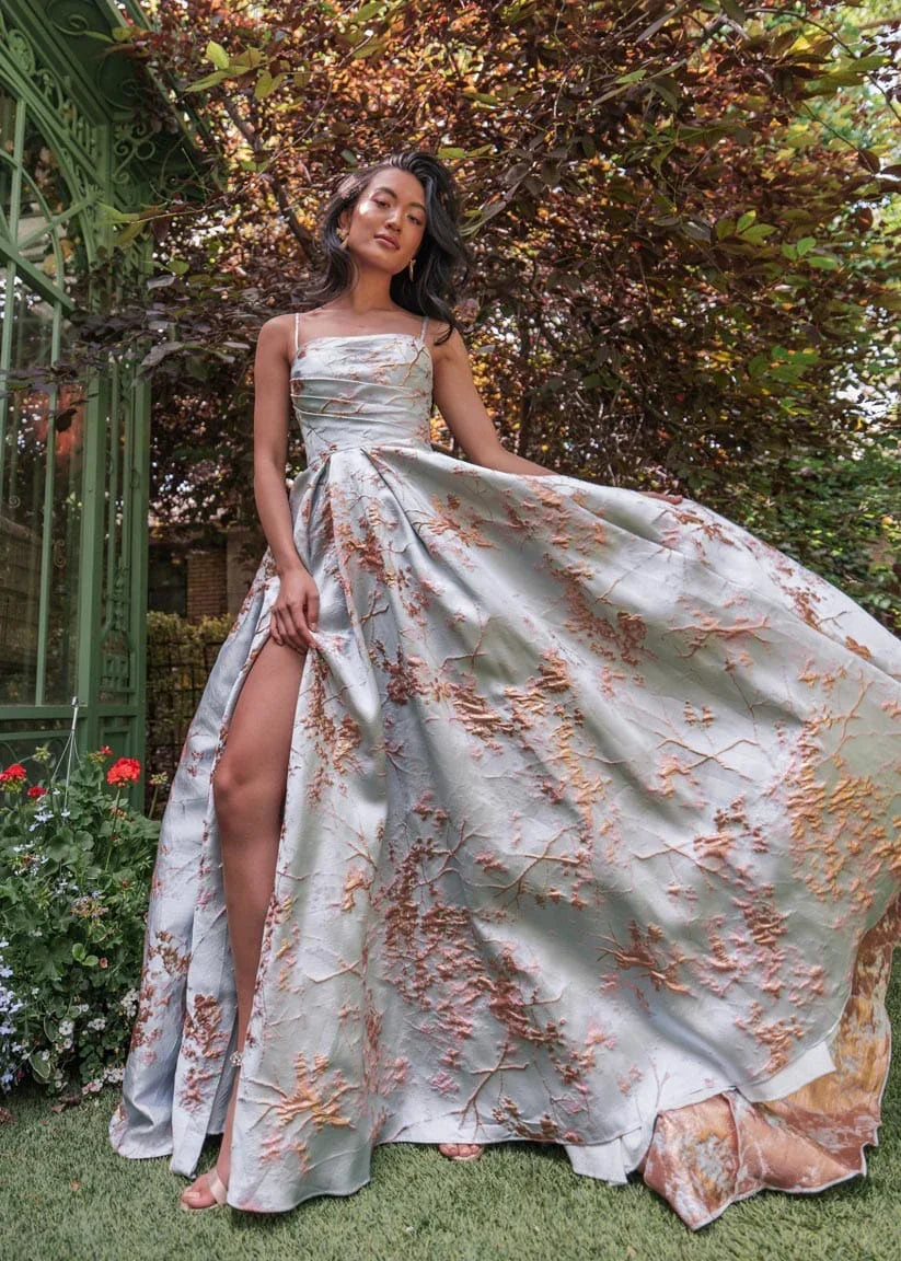 Blue Arabella Dress by JessaKae, featuring a flowing design with intricate details, displayed on a hanger.