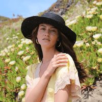 Straw hat from KIN THE LABEL's Resort Collection with wide brim and woven straw design, perfect for sunny outdoor wear.