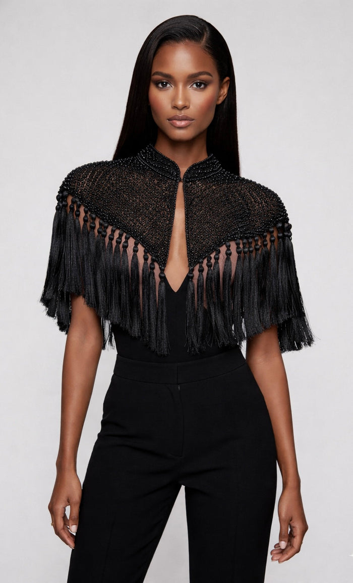 Black tassel cape by L'Jai Amor, featuring flowing fabric and decorative tassels, displayed on a neutral background.