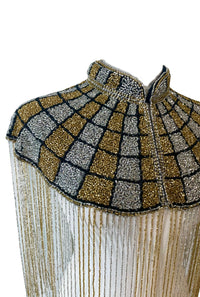 L'Jai Amor The Gilded Mosaic Cape displayed on a hanger, featuring intricate gold and mosaic patterns in luxurious fabric.