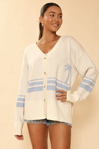 Miss Sparkling Ocean Sunset knit cardigan hanging on a wooden hanger, featuring a colorful ocean-inspired pattern and cozy knit texture.