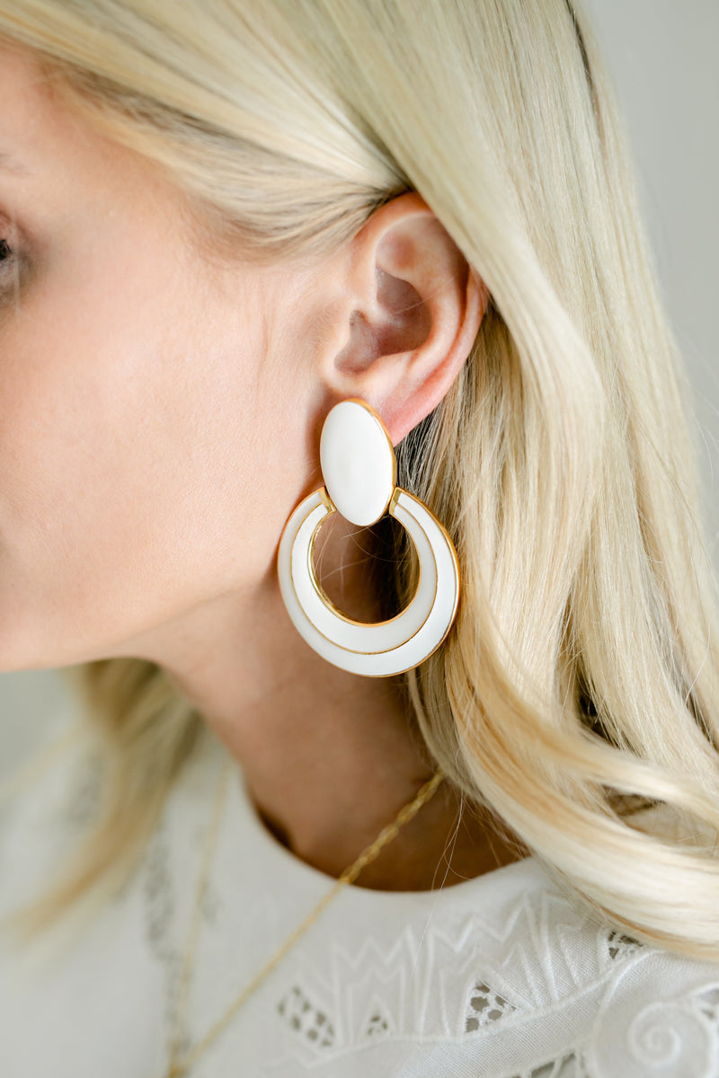White enamel circle jewelry piece by Modafleur, close-up of smooth, glossy round enamel surface on a neutral background.
