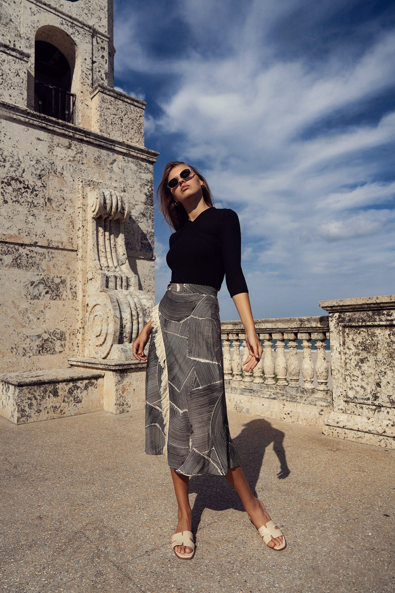 Faux wrap fringe skirt by Profile NYC featuring layered fringe design and lightweight fabric, shown in a stylish black color.