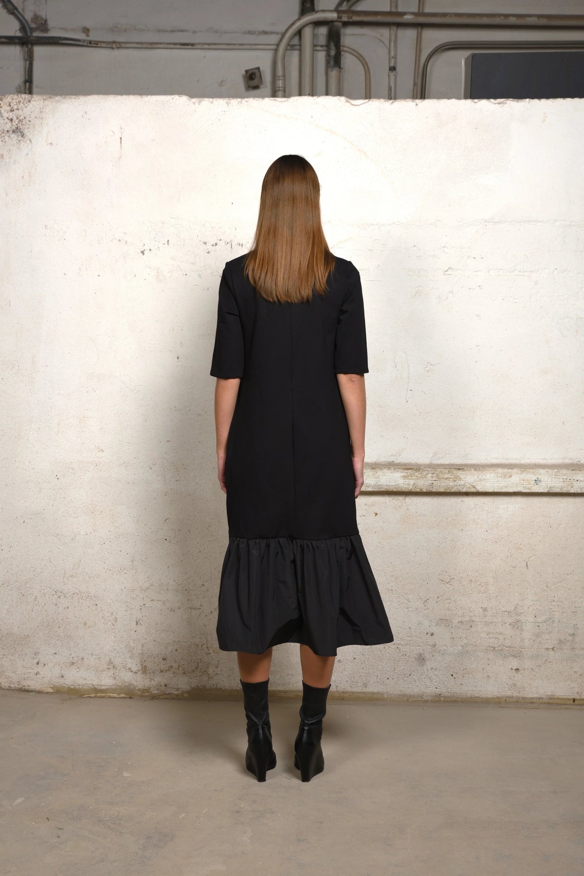 Back view of a Simply Mila unbalance ruffle sweater dress in soft knit fabric, featuring ruffle detailing at the hem.