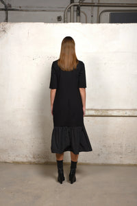 Back view of a Simply Mila unbalance ruffle sweater dress in soft knit fabric, featuring ruffle detailing at the hem.