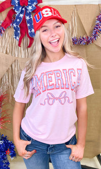 Pink America Frilly Bow graphic T-shirt by Sugar Stitch Wholesale featuring a playful bow design on soft cotton fabric.