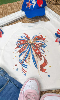 Edgy graphic shirt with patriotic ribbon bow design by Sugar Stitch Wholesale, featuring bold red, white, and blue colors.