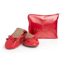 Red Talaria Flats shoes in ruby red color, positioned in front of a handbag, showcasing their stylish and comfortable design.