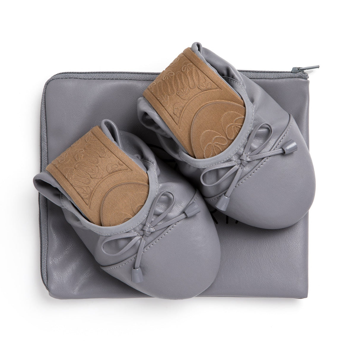 Talaria Flats premium stone grey shoes resting on a bag, showcasing their sleek design and comfortable slip-on style.