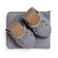 Talaria Flats premium stone grey shoes resting on a bag, showcasing their sleek design and comfortable slip-on style.