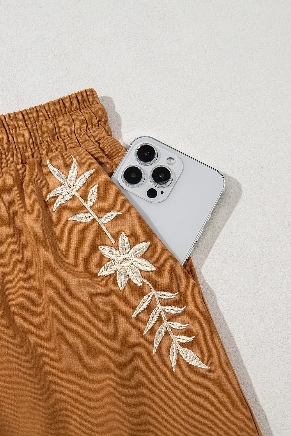 Embroidered boho-style casual shorts with tasseled drawstring and elastic waist, featuring trendy design and earthy caramel color.