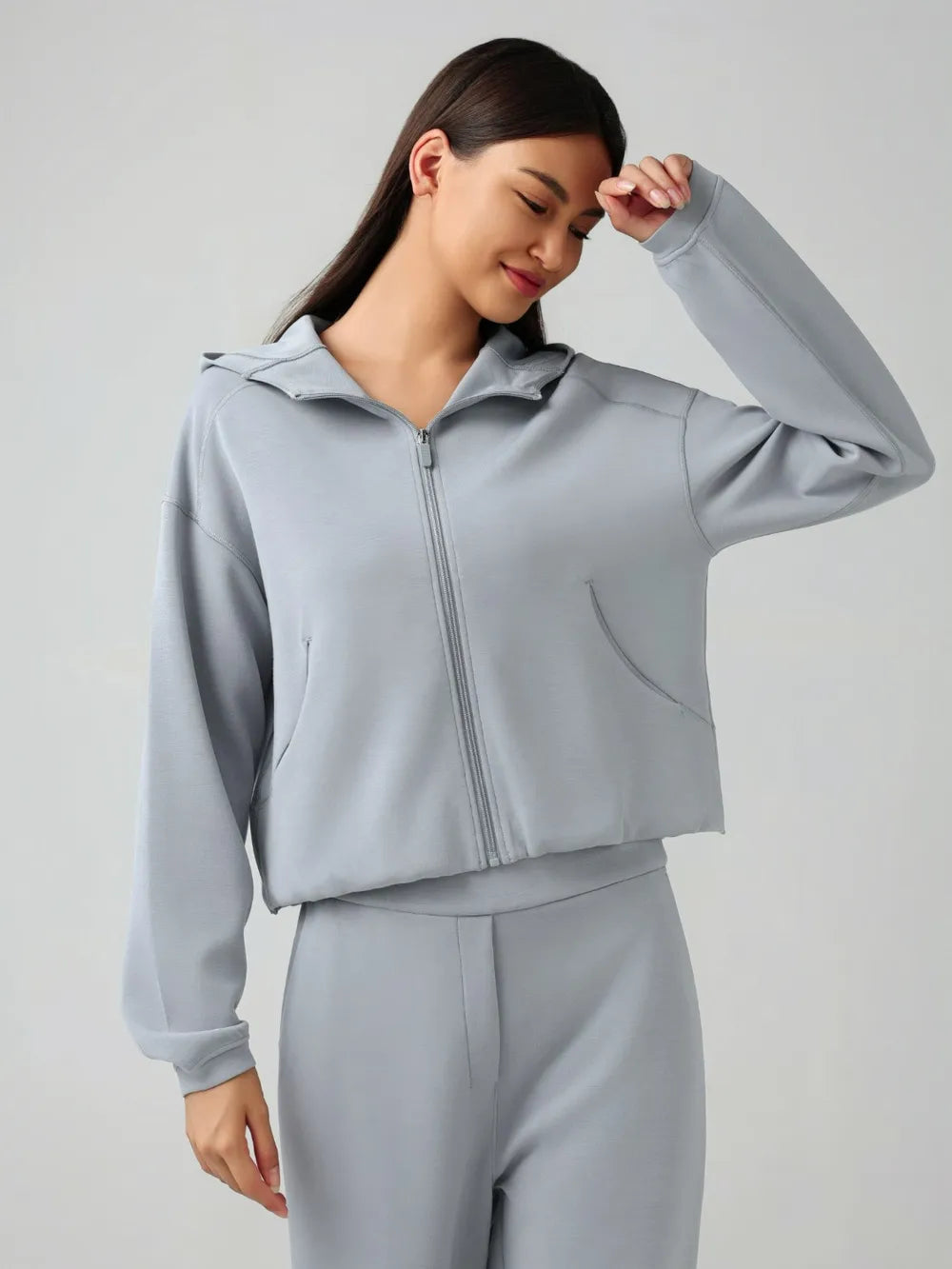 Trendsi Millennia zip-up active hoodie with dropped shoulders, hood, and front pockets, made of soft, comfortable fabric.