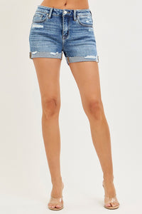 Risen mid-rise cuffed denim shorts with rolled hem and distressed details, styled with a casual top and accessories.