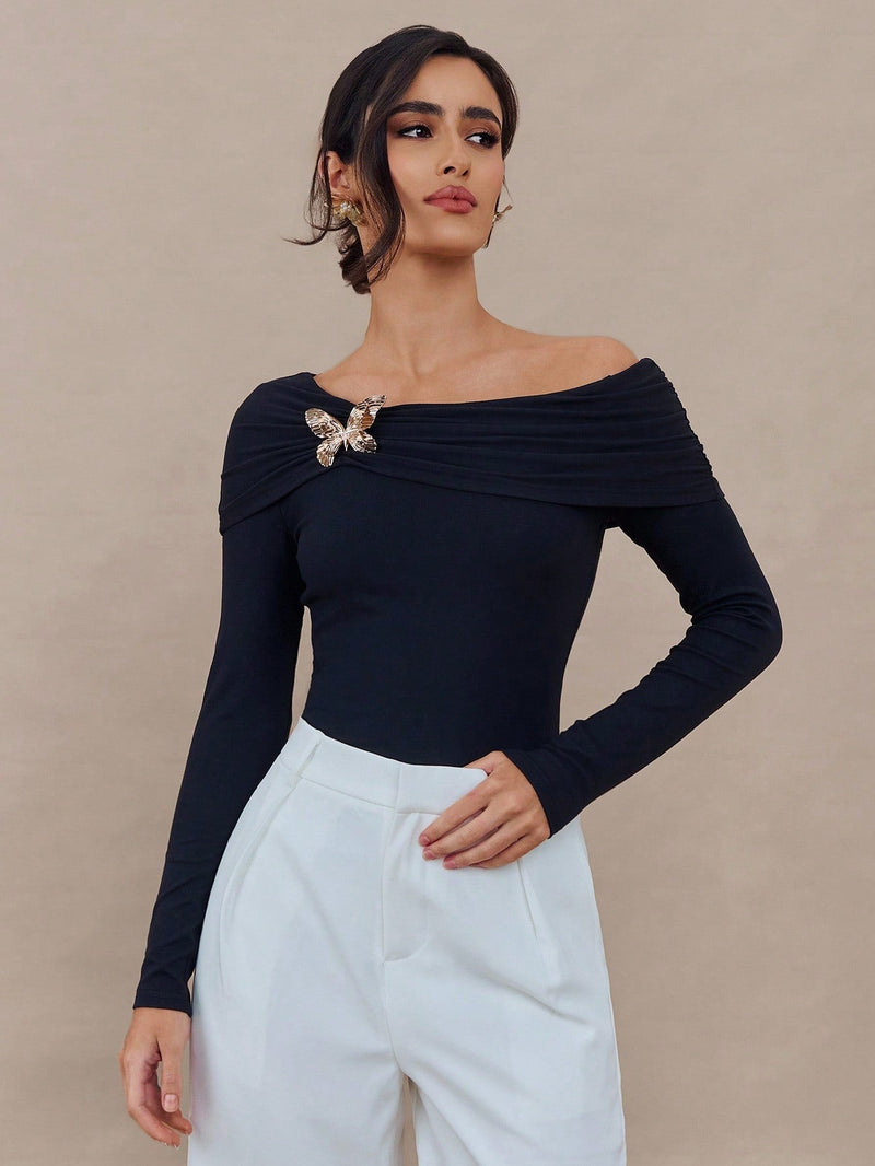 Black spring off-shoulder long-sleeved women’s top with butterfly brooch detail, slim fit, stylish design by Wanita Store.
