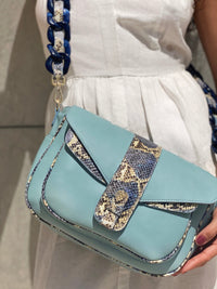 Ximena Kavalekas Kara blue leather crossbody bag with sleek design and adjustable strap, displayed on a neutral background.